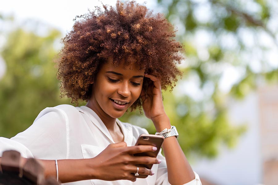 Contact Us - Young Woman in Professional Clothing Makes a Call on Her Gold Cell Phone Outside on a Sunny Day